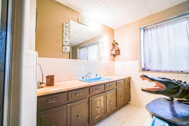 bathroom with tile walls, tasteful backsplash, a drop ceiling, tile patterned floors, and vanity