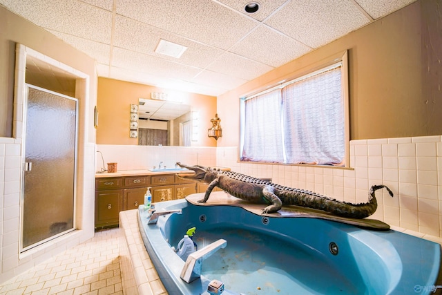 bathroom with a paneled ceiling, tile walls, separate shower and tub, tile patterned flooring, and vanity