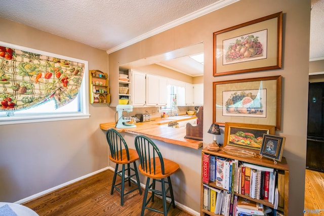 kitchen featuring a textured ceiling, white cabinetry, butcher block countertops, crown molding, and hardwood / wood-style flooring