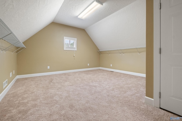 additional living space with a textured ceiling, vaulted ceiling, and light carpet