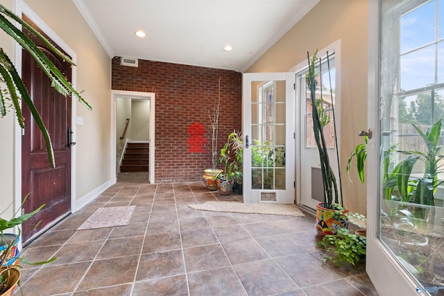 foyer entrance with tile patterned flooring, ornamental molding, and brick wall