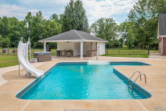 view of pool featuring a patio area, a water slide, a lawn, and a hot tub