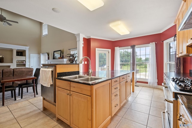 kitchen with light tile patterned flooring, sink, range with two ovens, decorative columns, and a center island with sink