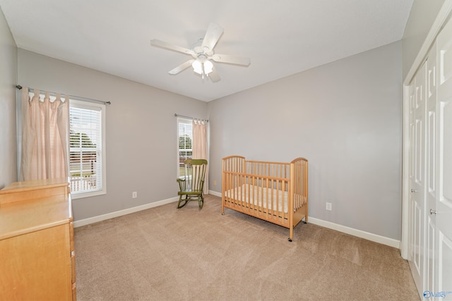 bedroom featuring a crib, ceiling fan, light colored carpet, and a closet