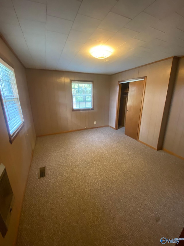 unfurnished bedroom featuring wood walls, a closet, and carpet flooring