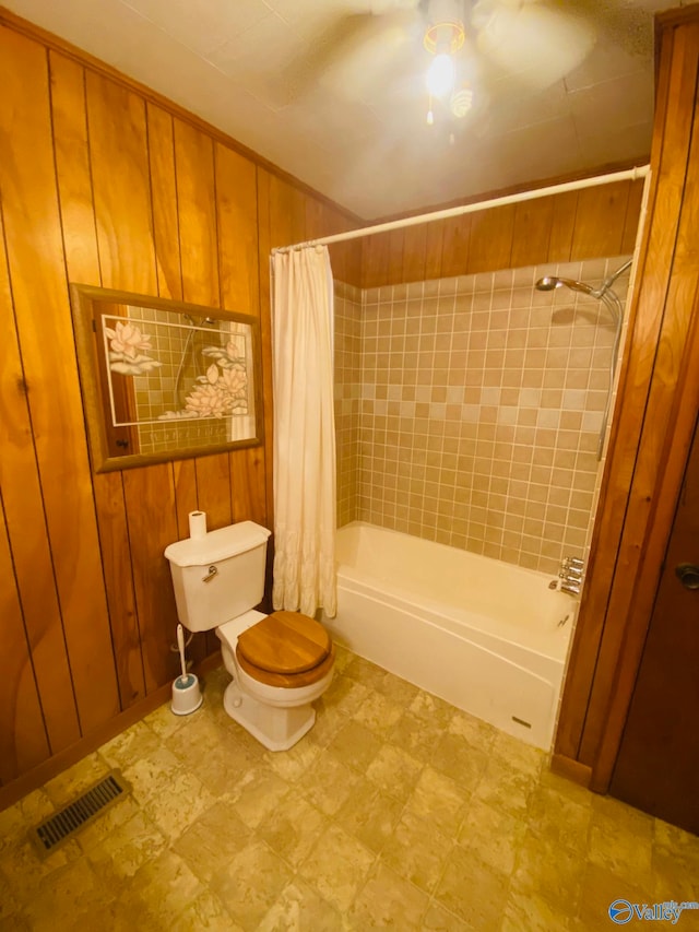 bathroom with wood walls, toilet, ceiling fan, and shower / bath combination with curtain