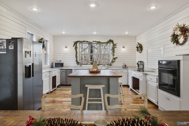 kitchen with a kitchen bar, appliances with stainless steel finishes, wood counters, a kitchen island, and white cabinetry