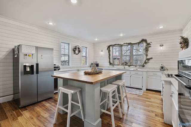 kitchen with a center island, stainless steel fridge with ice dispenser, white cabinetry, butcher block counters, and a breakfast bar area