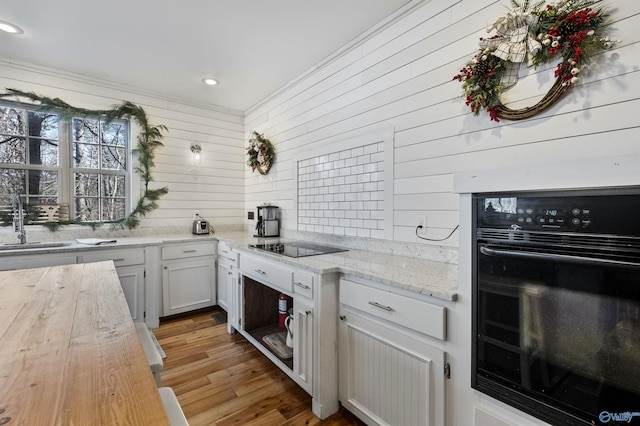 kitchen featuring wooden walls, sink, black appliances, light hardwood / wood-style flooring, and white cabinets