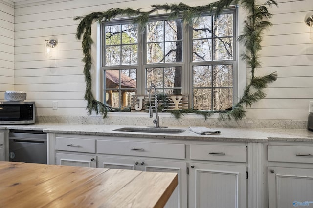 bar featuring wooden walls, sink, white cabinets, and light stone countertops