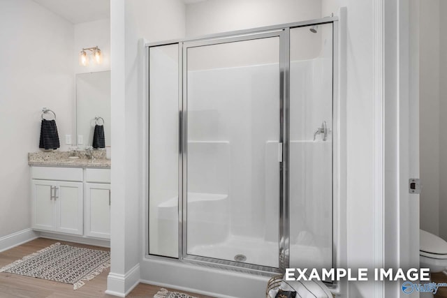 bathroom with toilet, a shower stall, vanity, and wood finished floors