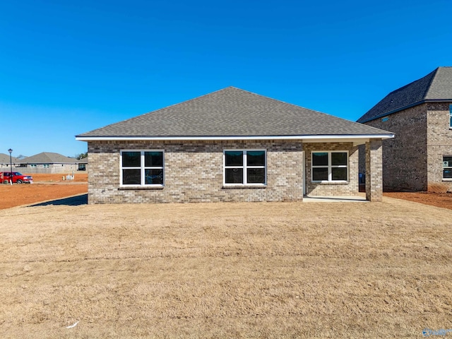 back of house featuring brick siding and roof with shingles