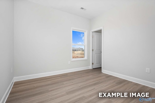 empty room featuring wood finished floors, visible vents, and baseboards