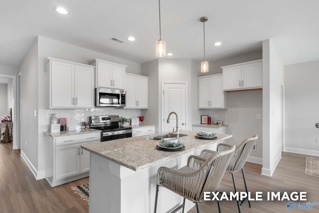 kitchen featuring appliances with stainless steel finishes, white cabinets, a sink, an island with sink, and baseboards