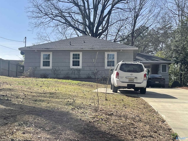 view of property exterior with roof with shingles, driveway, and fence