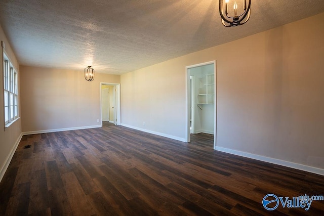 spare room with dark hardwood / wood-style flooring, a textured ceiling, and a notable chandelier