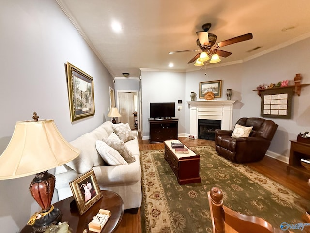 living area featuring ceiling fan, a fireplace, wood finished floors, and crown molding