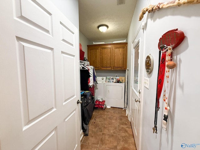 washroom featuring a textured ceiling, washing machine and dryer, cabinet space, and tile patterned floors