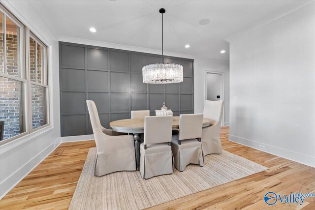 dining room featuring crown molding, light wood-style flooring, a decorative wall, and an inviting chandelier