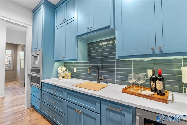 kitchen featuring a sink, backsplash, oven, and blue cabinets