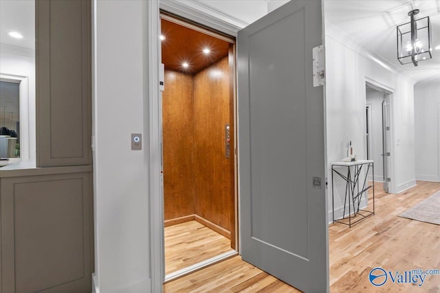 hallway with a chandelier, elevator, wood finished floors, and crown molding