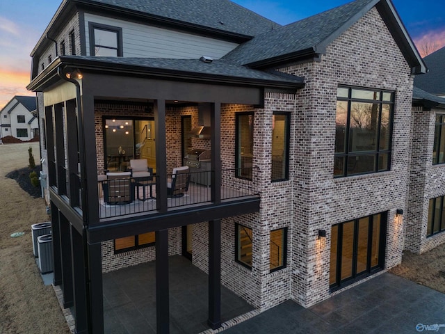 back of property featuring brick siding, roof with shingles, a patio area, and central air condition unit