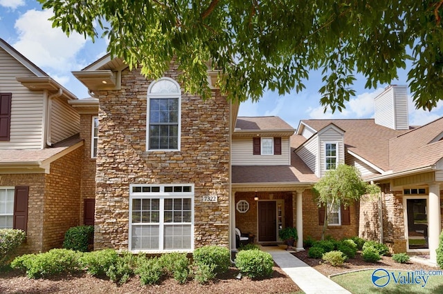 traditional-style home featuring a shingled roof, stone siding, and brick siding