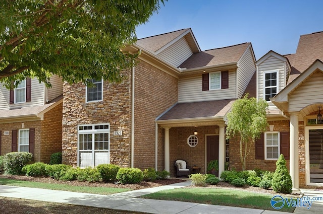 townhome / multi-family property with stone siding, brick siding, and roof with shingles