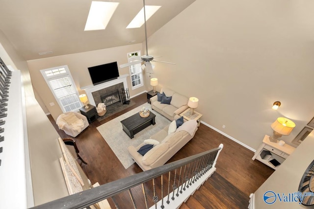 living room with lofted ceiling with skylight, ceiling fan, wood finished floors, a tile fireplace, and baseboards