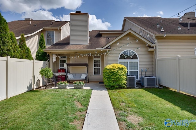 back of house featuring central AC, a lawn, and a fenced backyard