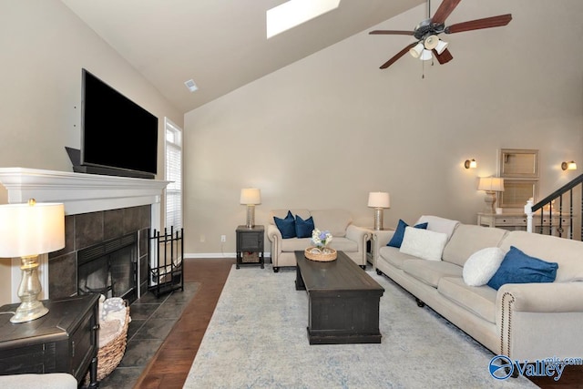 living area with baseboards, a tiled fireplace, wood finished floors, stairs, and high vaulted ceiling