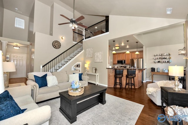 living room with dark wood-style floors, ceiling fan, high vaulted ceiling, baseboards, and stairs