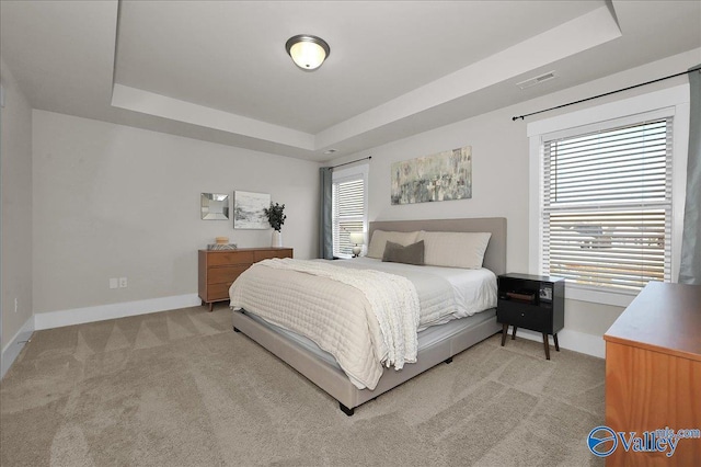 bedroom featuring visible vents, a raised ceiling, and light carpet