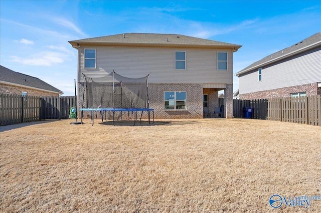 rear view of property with a yard, a trampoline, a fenced backyard, and brick siding