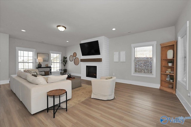 living room featuring recessed lighting, a fireplace, light wood-type flooring, and baseboards