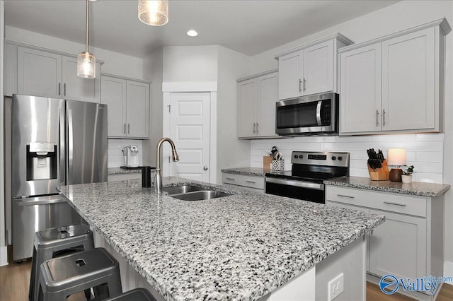 kitchen featuring light stone countertops, a kitchen island with sink, a sink, appliances with stainless steel finishes, and tasteful backsplash