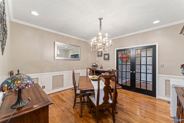 dining space with a chandelier, french doors, crown molding, and light wood-type flooring