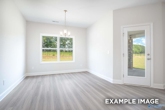 unfurnished room featuring baseboards, wood finished floors, visible vents, and a notable chandelier