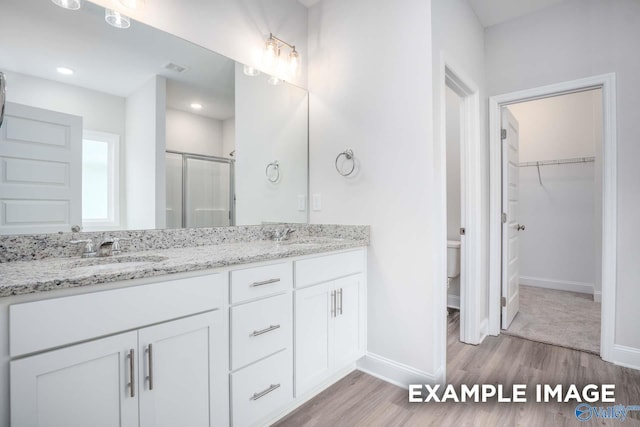 bathroom with wood finished floors, a sink, baseboards, a shower stall, and double vanity