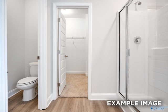 bathroom featuring toilet, a stall shower, a walk in closet, and wood finished floors