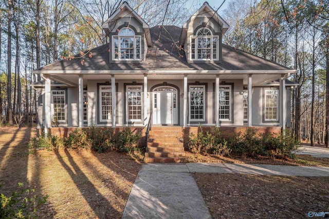 view of front of property featuring stucco siding, a shingled roof, a porch, and brick siding