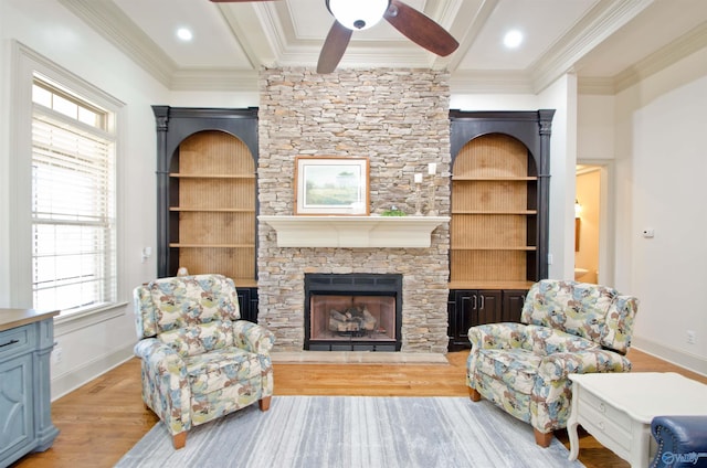 living room with wood finished floors, baseboards, beam ceiling, a stone fireplace, and crown molding