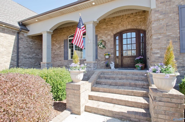 view of exterior entry featuring brick siding, a porch, and a shingled roof