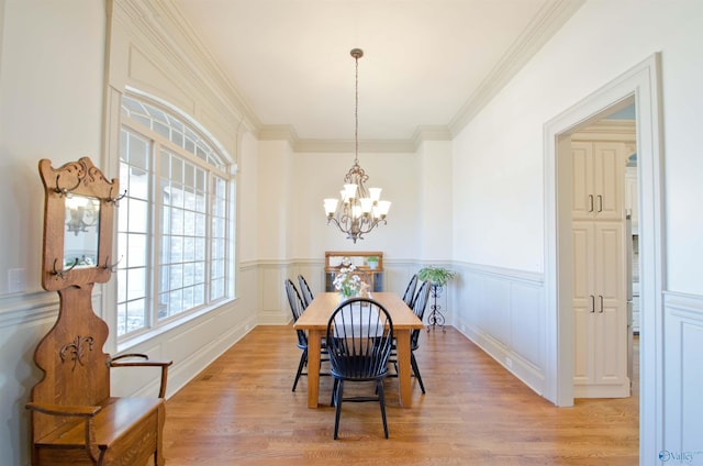 dining area featuring an inviting chandelier, ornamental molding, light wood-style floors, wainscoting, and a decorative wall