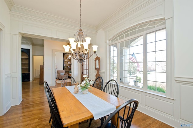 dining area featuring crown molding, a decorative wall, light wood-type flooring, and a chandelier