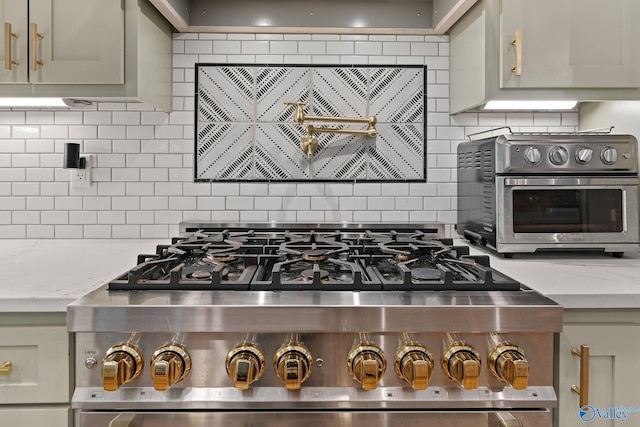 kitchen with light stone countertops, tasteful backsplash, gray cabinets, and stainless steel range oven