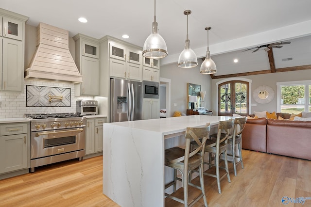 kitchen with custom range hood, stainless steel appliances, hanging light fixtures, and light hardwood / wood-style flooring