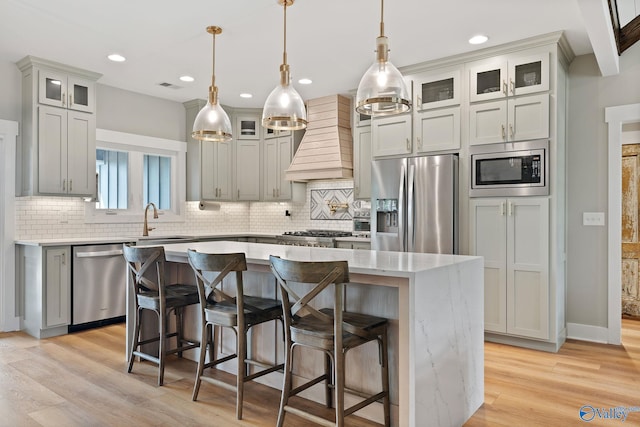 kitchen featuring a kitchen island, custom range hood, appliances with stainless steel finishes, and light hardwood / wood-style flooring