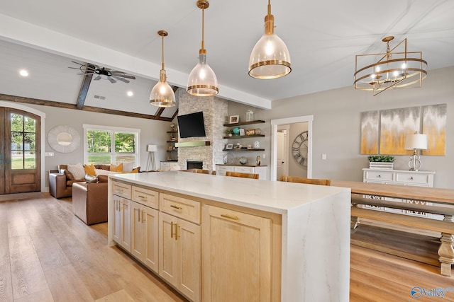 kitchen featuring light wood-type flooring, ceiling fan with notable chandelier, decorative light fixtures, a fireplace, and a center island