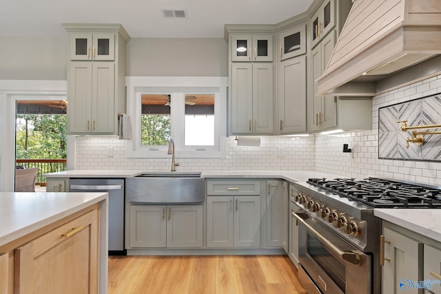 kitchen featuring custom exhaust hood, backsplash, sink, light hardwood / wood-style flooring, and appliances with stainless steel finishes